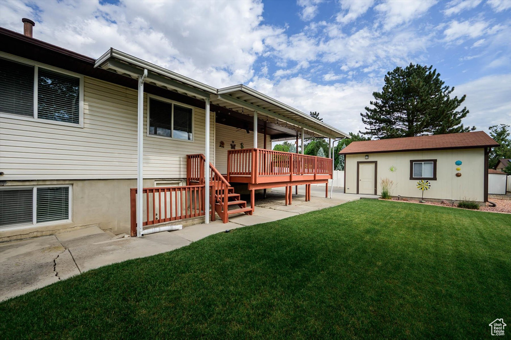 Rear view of property featuring a yard, a deck, an outbuilding, and a patio