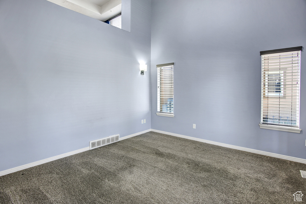 Unfurnished room featuring dark carpet, a towering ceiling, and plenty of natural light