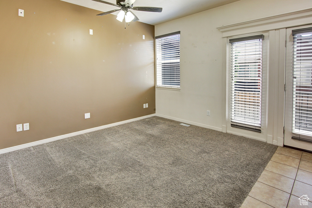 Carpeted empty room with a ceiling fan and tile patterned floors