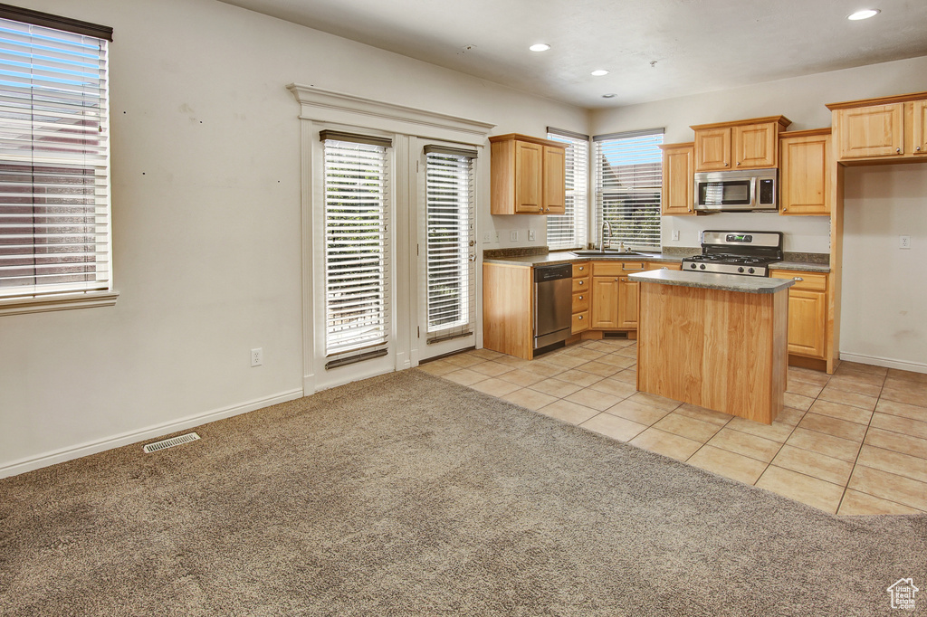 Kitchen featuring stainless steel appliances, recessed lighting, light tile patterned floors, a center island, and light carpet