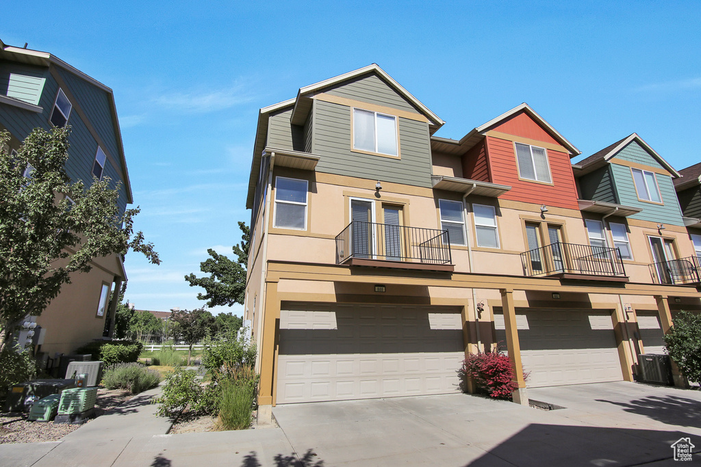 Townhome / multi-family property with concrete driveway, stucco siding, a garage, and a balcony