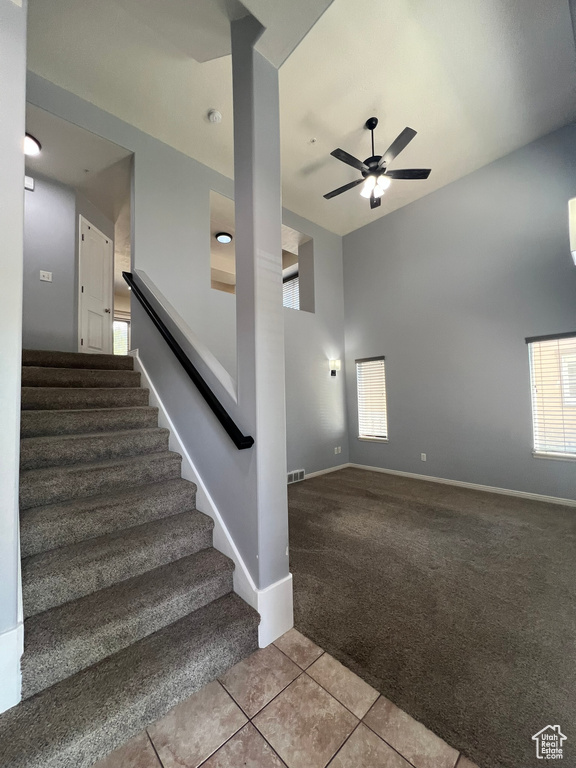 Stairs with carpet, tile patterned flooring, ceiling fan, and a high ceiling