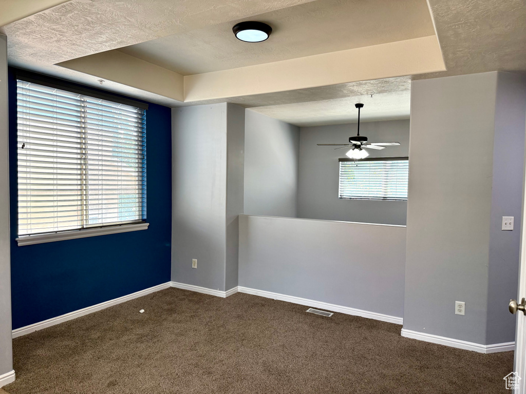 Empty room with a ceiling fan, a raised ceiling, and carpet flooring