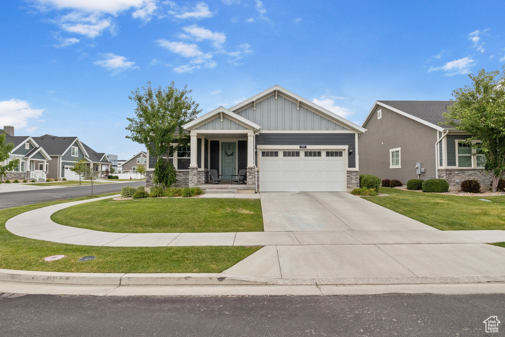 Craftsman-style house featuring stone siding, a front lawn, driveway, and a garage