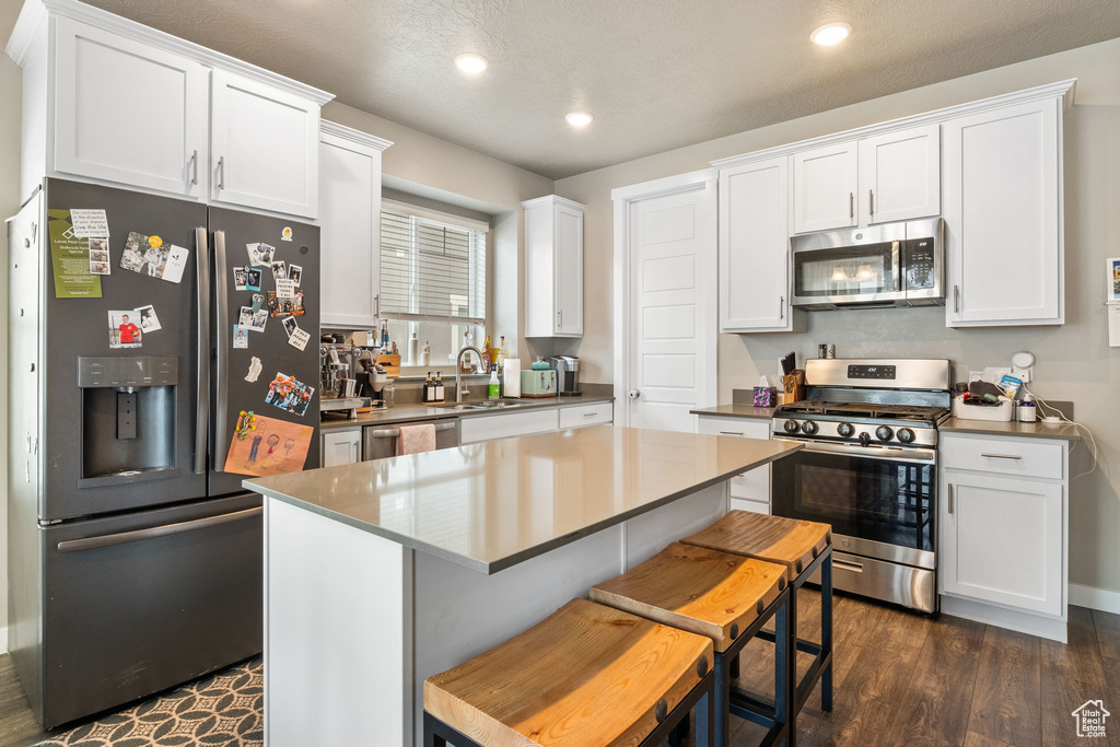 Kitchen with stainless steel appliances, white cabinetry, recessed lighting, dark wood-style flooring, and a kitchen island