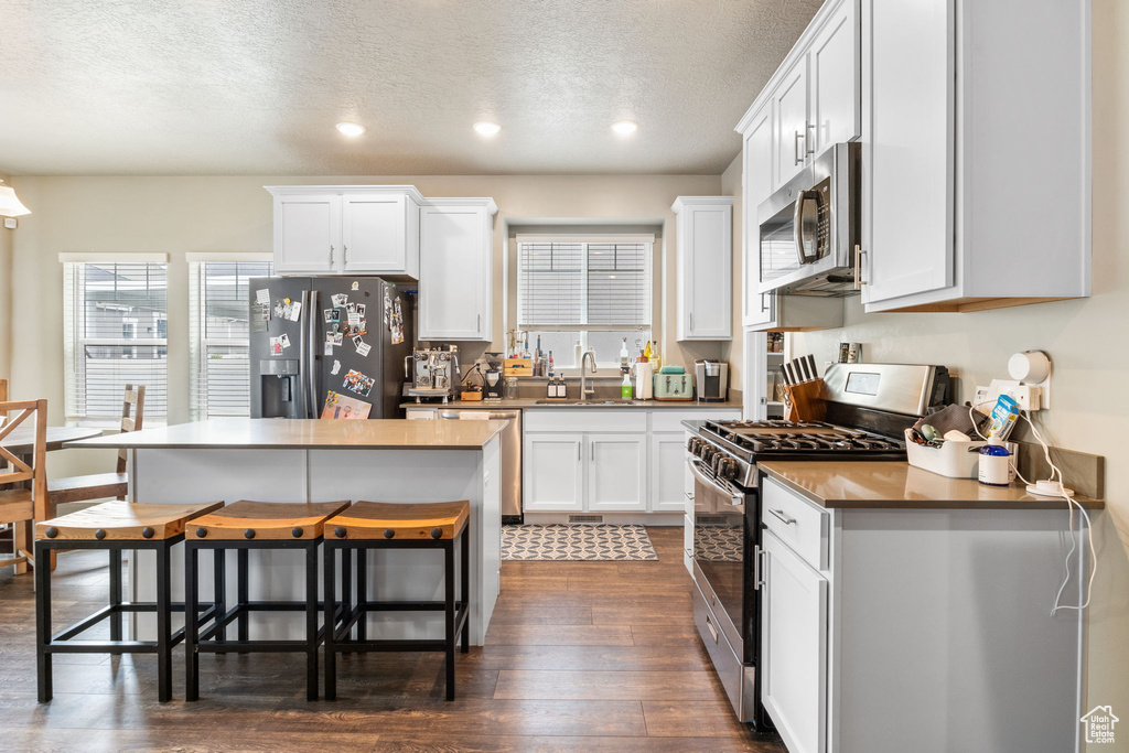 Kitchen featuring stainless steel appliances, dark wood-type flooring, a kitchen breakfast bar, a textured ceiling, and recessed lighting