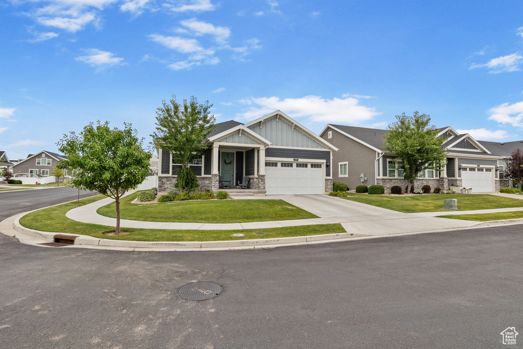 Craftsman inspired home featuring stone siding, a garage, a front lawn, driveway, and board and batten siding