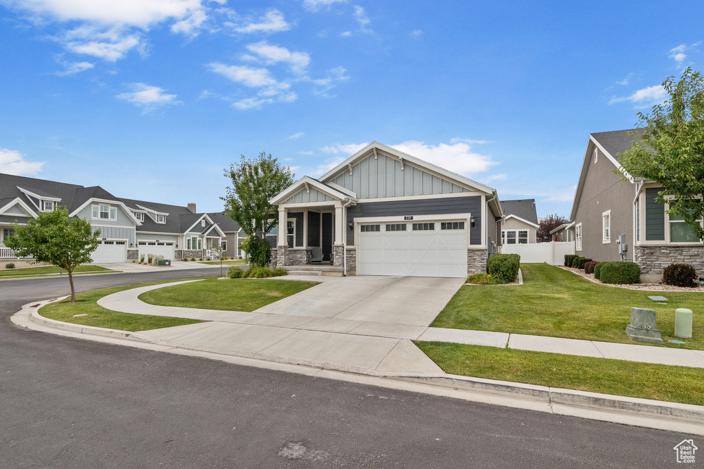 Craftsman-style home with board and batten siding, stone siding, concrete driveway, a garage, and a residential view