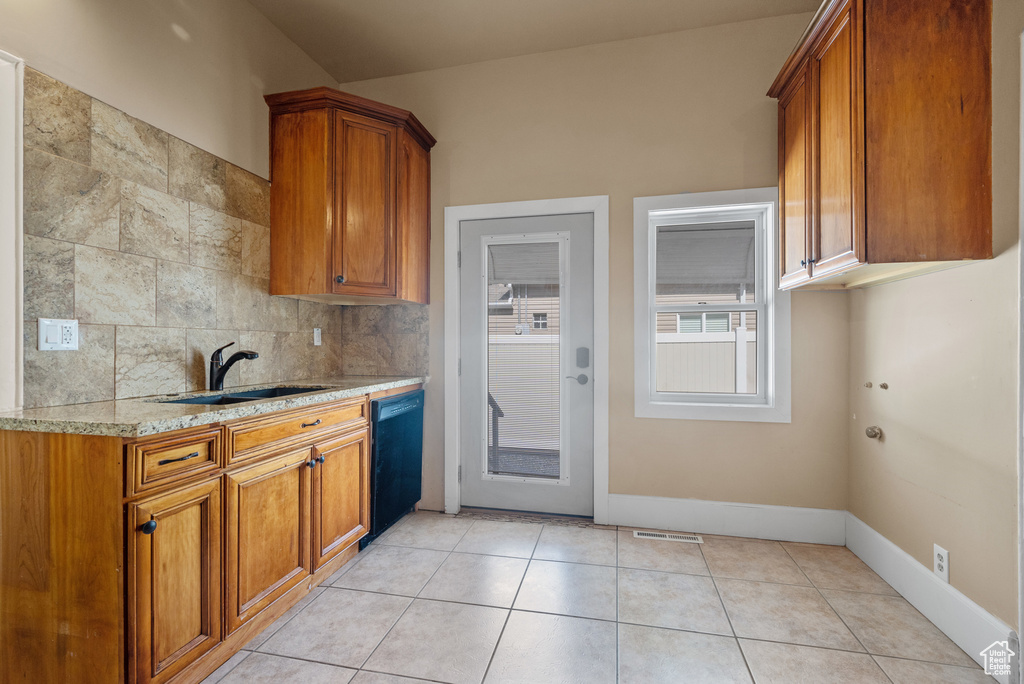 Kitchen with dishwasher, brown cabinets, light stone counters, and backsplash