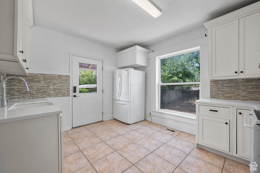 Kitchen with freestanding refrigerator, light tile patterned floors, decorative backsplash, and white cabinets
