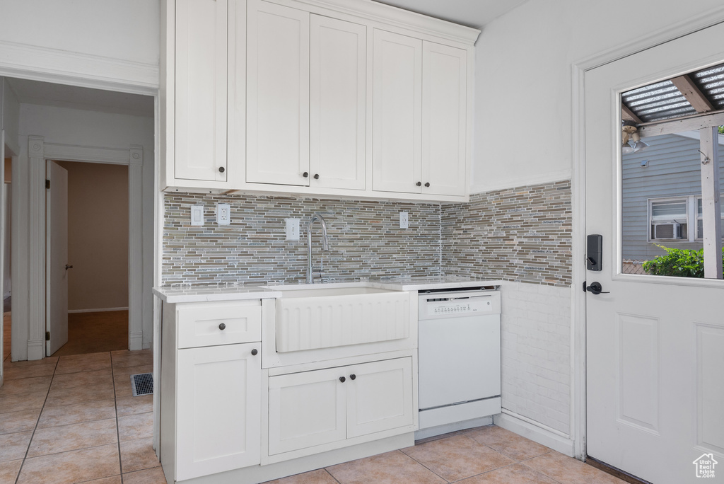 Kitchen with white dishwasher, light countertops, light tile patterned flooring, decorative backsplash, and white cabinets