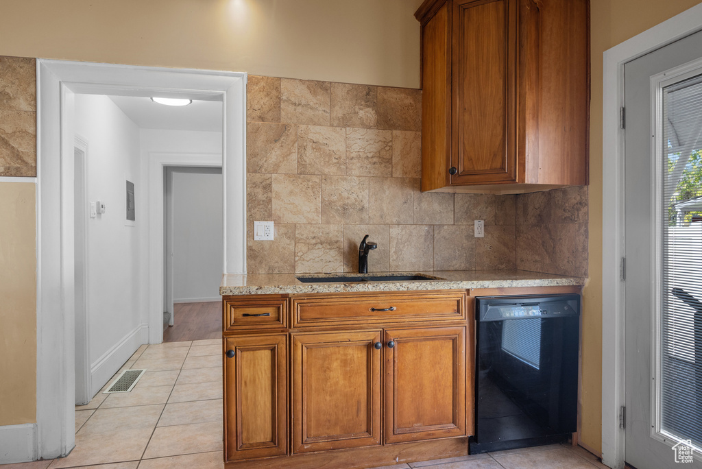 Kitchen featuring black dishwasher, brown cabinetry, backsplash, and light tile patterned floors