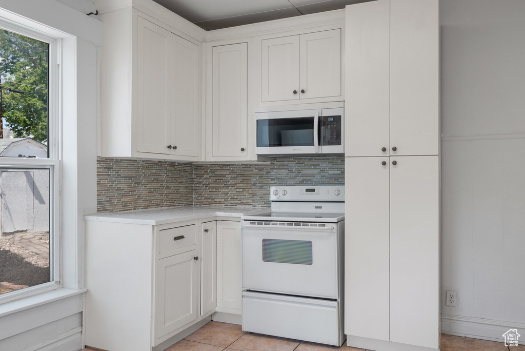 Kitchen with electric range, light countertops, tasteful backsplash, and white cabinets