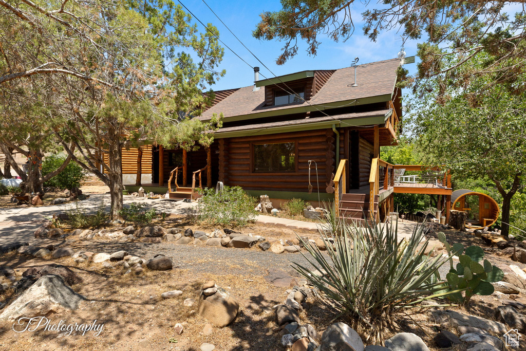View of front of house with log exterior, a wooden deck, and a shingled roof