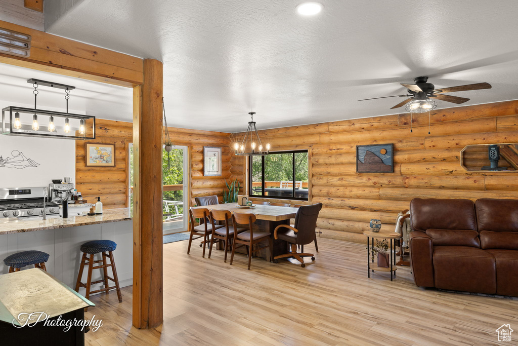 Dining room with a chandelier, light wood-type flooring, a ceiling fan, and log walls