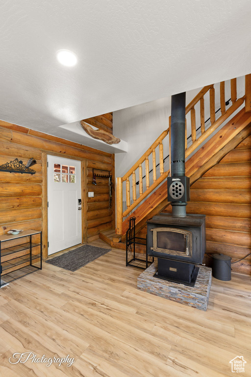 Entryway with rustic walls, stairs, wood finished floors, and a wood stove