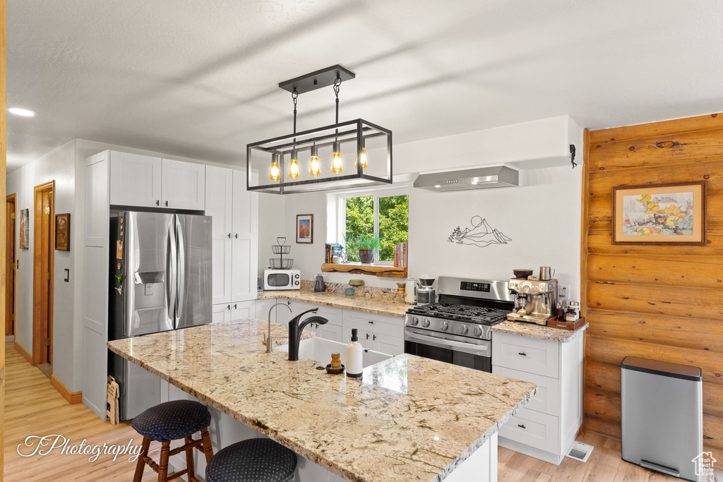 Kitchen with stainless steel appliances, light wood finished floors, white cabinetry, light stone counters, and a breakfast bar