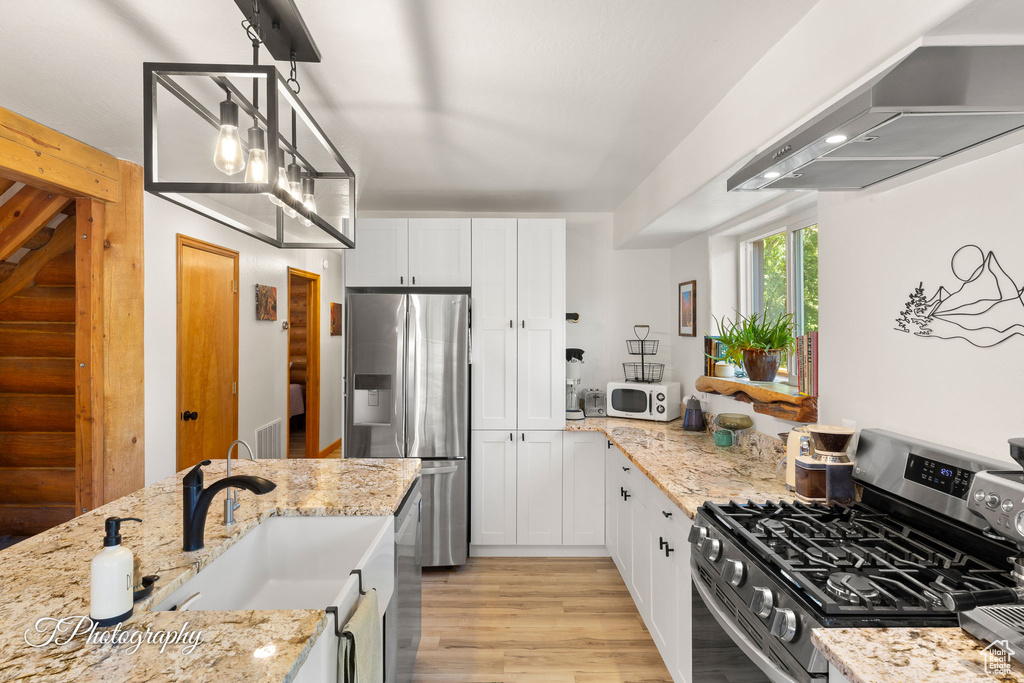 Kitchen featuring stainless steel appliances, extractor fan, white cabinetry, and light stone countertops