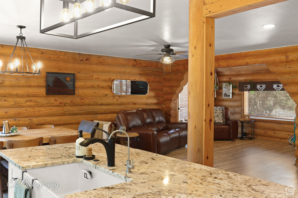Kitchen featuring rustic walls, a chandelier, open floor plan, wood finished floors, and light stone countertops