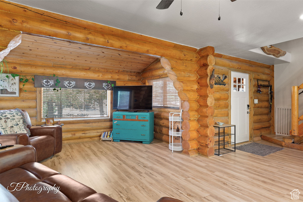 Living room with log walls, wood finished floors, ceiling fan, and stairs