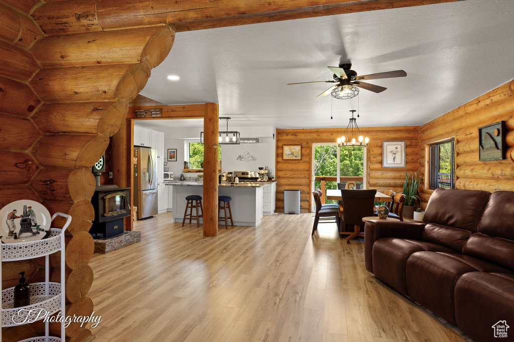 Living area featuring a ceiling fan, rustic walls, a wood stove, light wood-type flooring, and a chandelier
