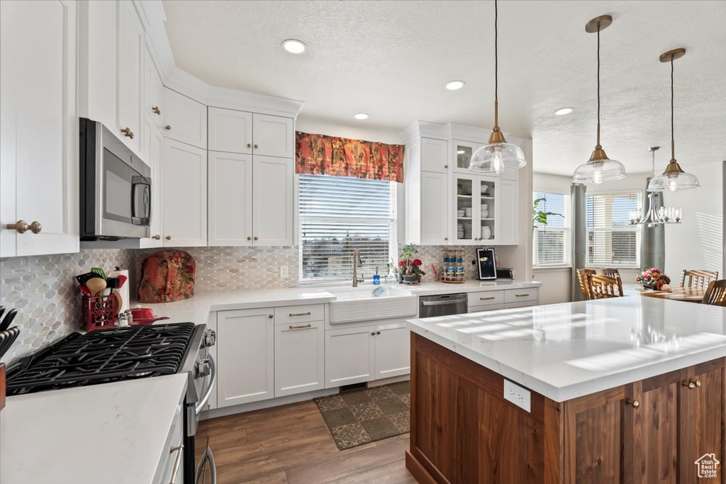 Kitchen featuring stainless steel appliances, dark wood-style flooring, light countertops, a kitchen island, and white cabinets