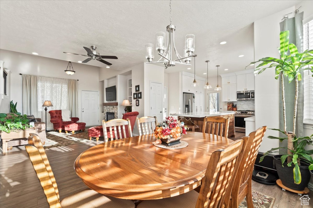 Dining area with healthy amount of natural light, wood finished floors, ceiling fan, a chandelier, and a textured ceiling