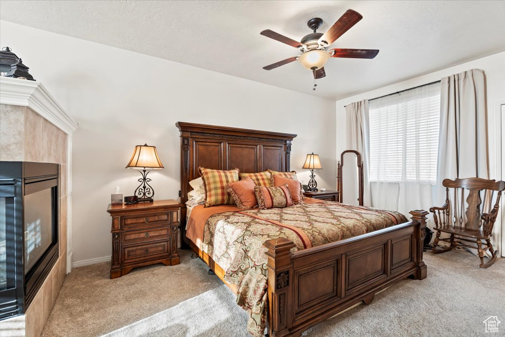 Bedroom with light colored carpet, a tiled fireplace, and ceiling fan