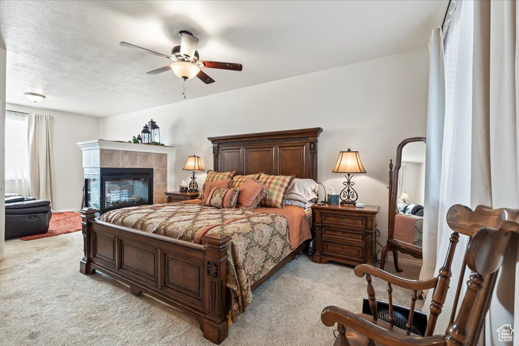 Bedroom with light carpet, a tiled fireplace, and a ceiling fan