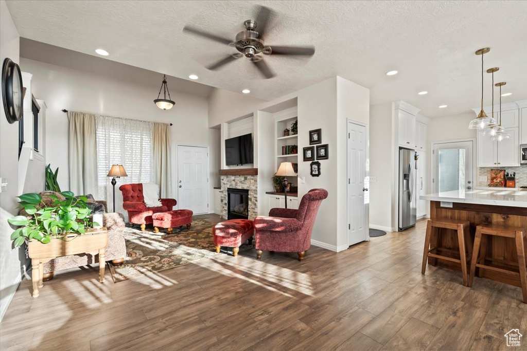 Living area featuring a fireplace, ceiling fan, wood finished floors, a textured ceiling, and recessed lighting