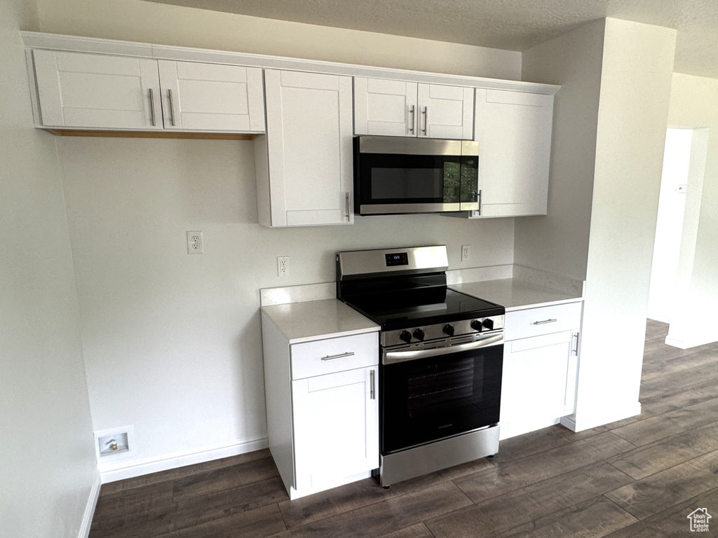 Kitchen with appliances with stainless steel finishes, dark wood-style floors, white cabinets, and light countertops