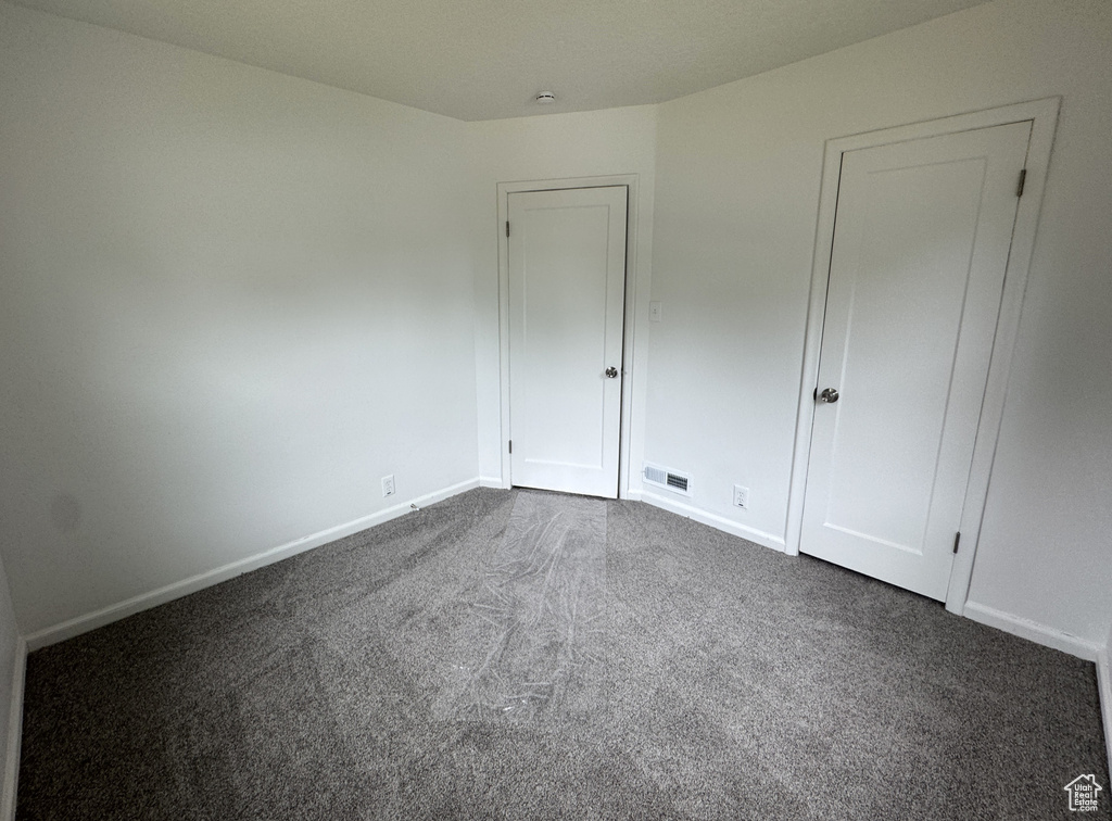 Unfurnished bedroom with dark colored carpet and baseboards