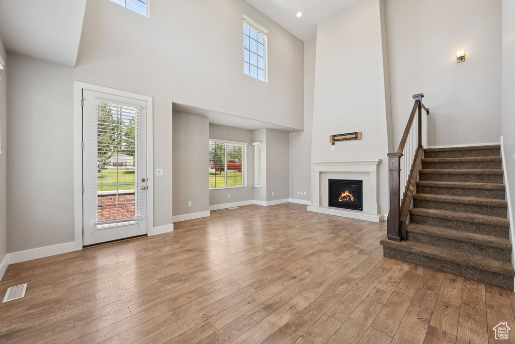 Unfurnished living room featuring a towering ceiling, hardwood / wood-style flooring, stairs, and a glass covered fireplace