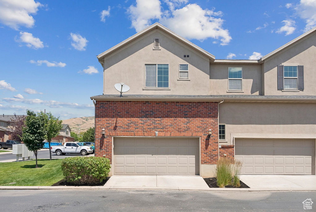 View of front of house with an attached garage, stucco siding, brick siding, and driveway