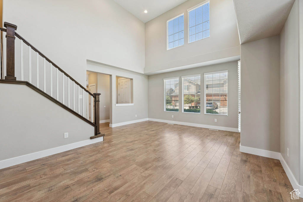 Unfurnished living room featuring a high ceiling, light wood-type flooring, stairway, and recessed lighting
