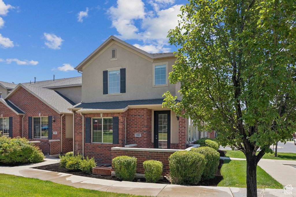 Traditional home featuring stucco siding, brick siding, a front lawn, and roof with shingles