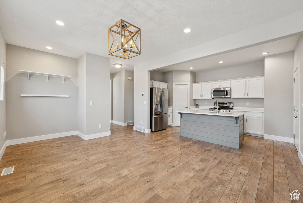Kitchen with appliances with stainless steel finishes, light countertops, white cabinets, light wood-style floors, and recessed lighting