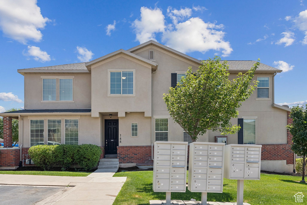 Townhome / multi-family property with brick siding, stucco siding, and a front yard