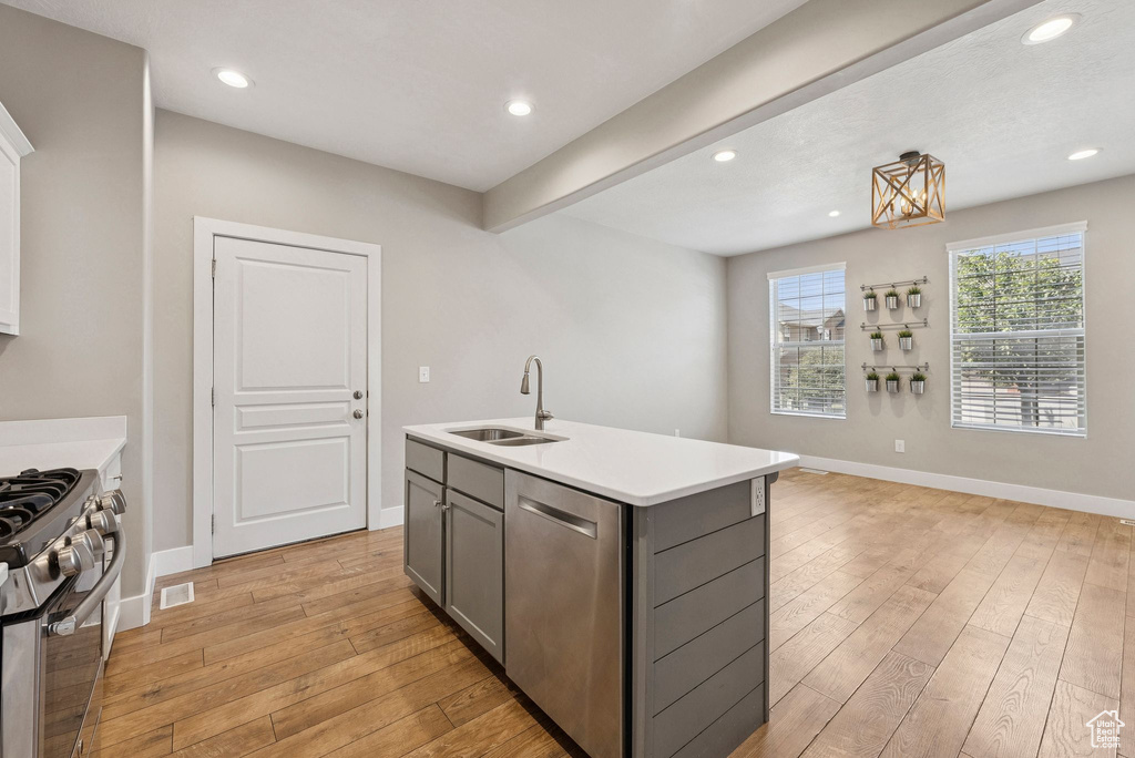 Kitchen featuring stainless steel appliances, gray cabinetry, light countertops, light wood-style floors, and a center island with sink