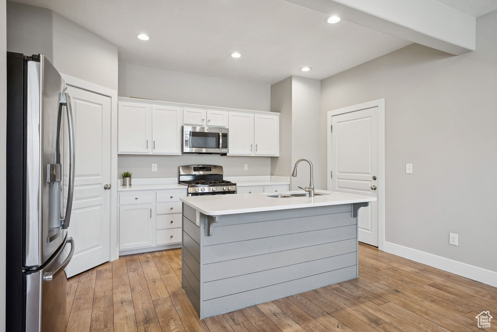 Kitchen with appliances with stainless steel finishes, white cabinets, an island with sink, light wood-type flooring, and light countertops