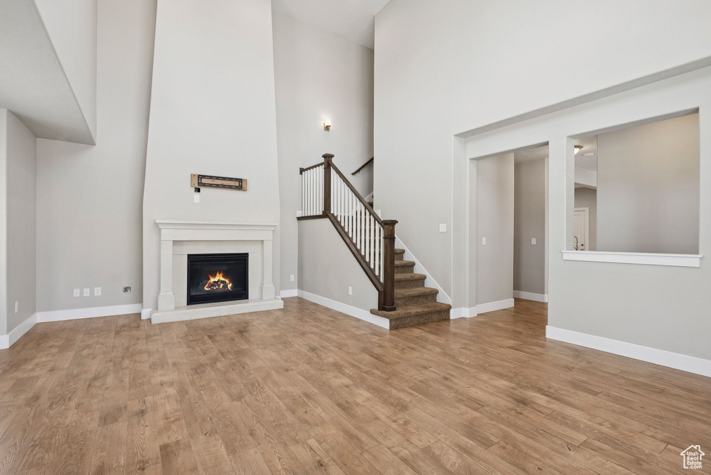 Unfurnished living room with light wood finished floors, a towering ceiling, a warm lit fireplace, and stairway