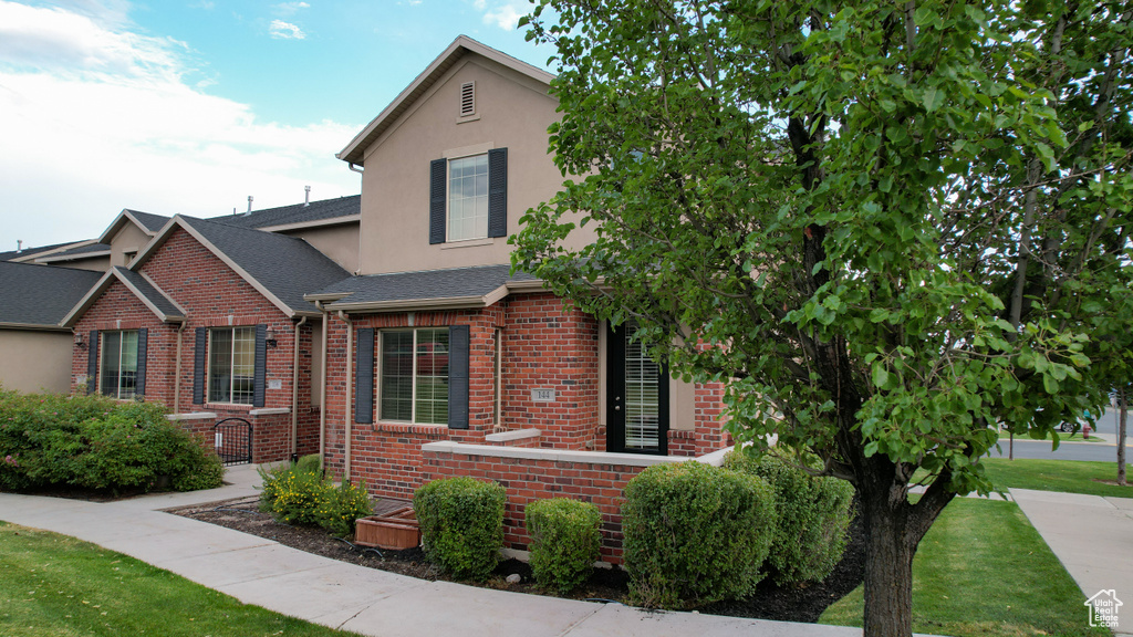 Traditional-style home with brick siding, stucco siding, a front lawn, and a shingled roof