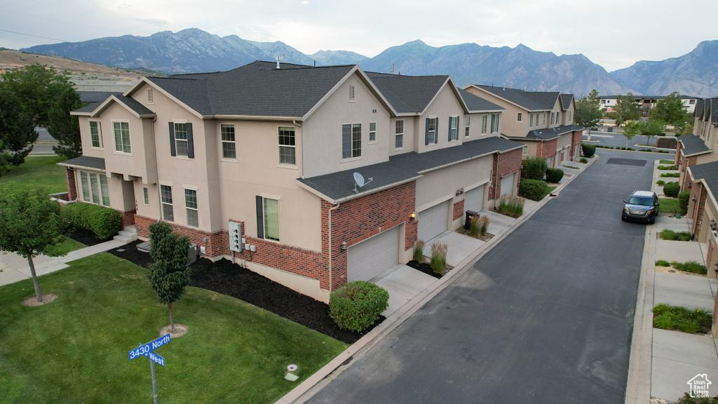 View of front of home with stucco siding, brick siding, an attached garage, a mountain view, and a front yard