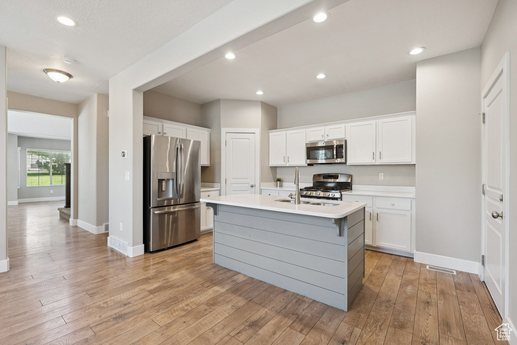 Kitchen with appliances with stainless steel finishes, light countertops, white cabinets, light wood-style floors, and recessed lighting