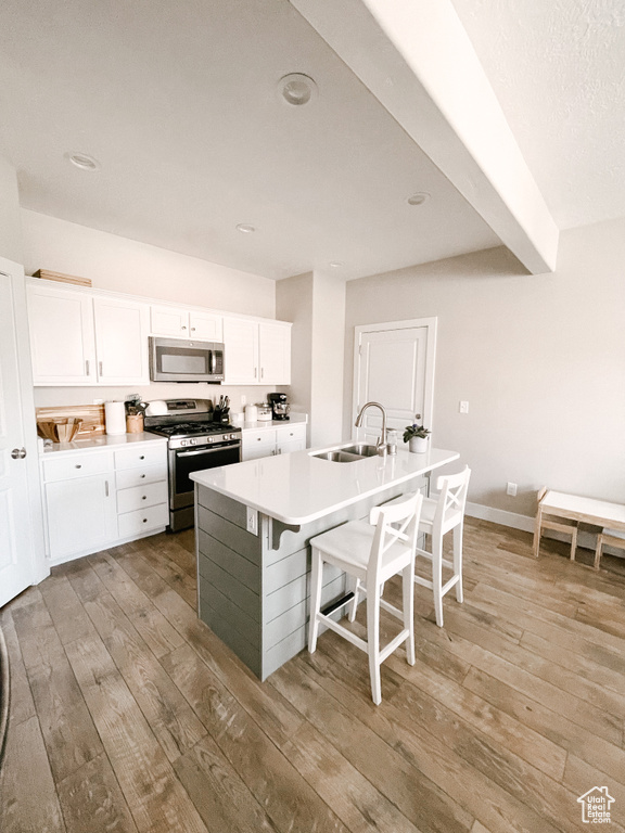 Kitchen featuring stainless steel appliances, light wood-type flooring, white cabinetry, a center island with sink, and a breakfast bar
