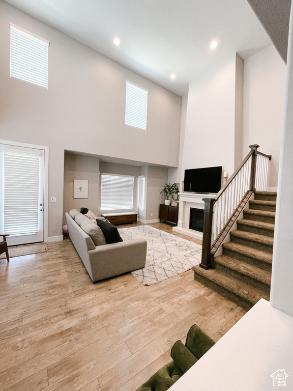 Living area featuring a high ceiling, wood finished floors, stairs, a fireplace with raised hearth, and recessed lighting