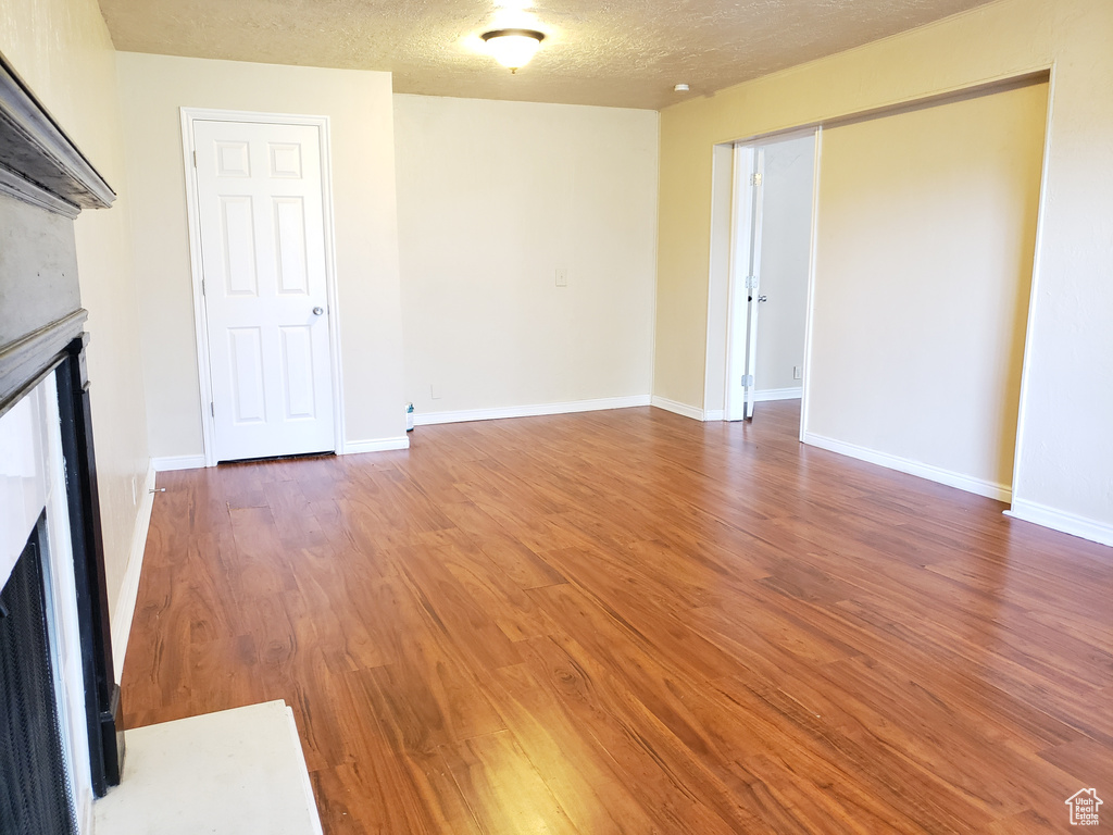 Unfurnished living room featuring a fireplace, wood finished floors, and a textured ceiling