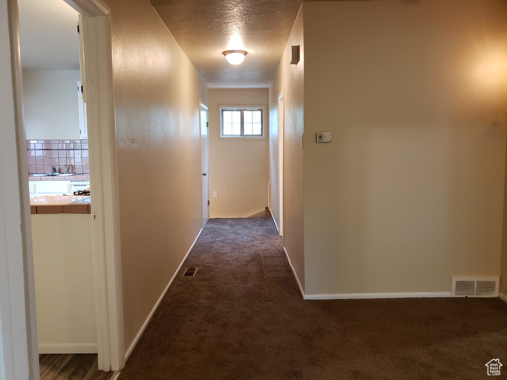 Hall featuring dark carpet and a textured ceiling