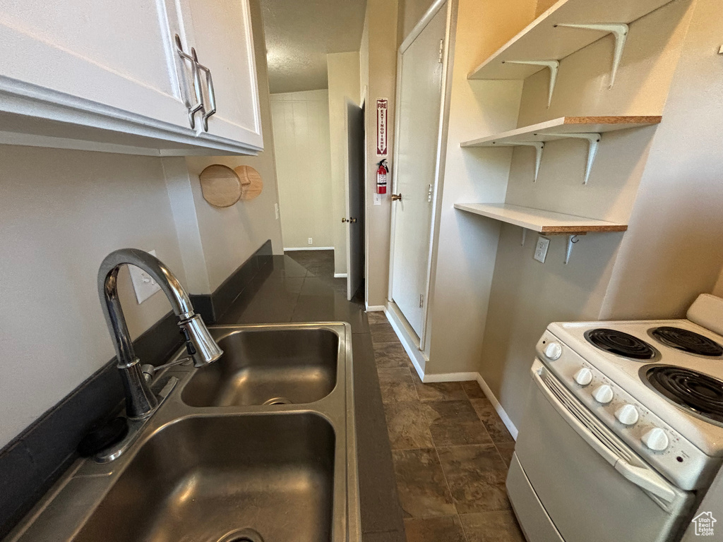 Kitchen featuring electric range, white cabinetry, open shelves, and dark stone finish floors