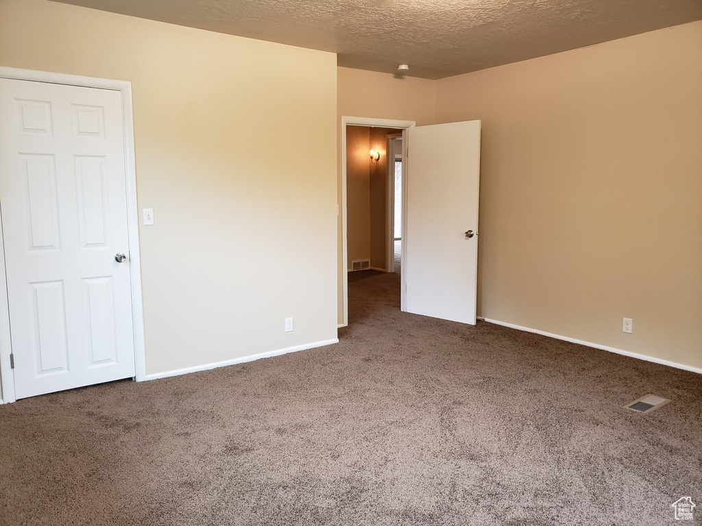 Carpeted empty room with a textured ceiling and baseboards